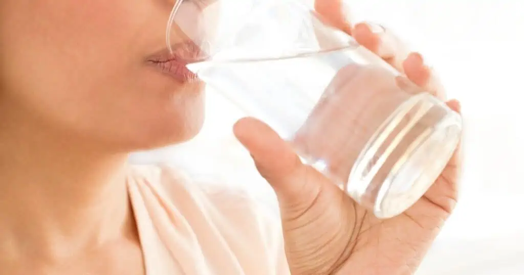 Hier drinkt een vrouw een glas water om goed gehydrateerd te blijven